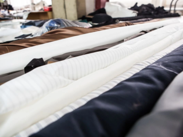 Rolls of different fabric materials, including cotton, polyester, and blended textiles, displayed in a workshop, highlighting texture and finish differences for fabric selection.