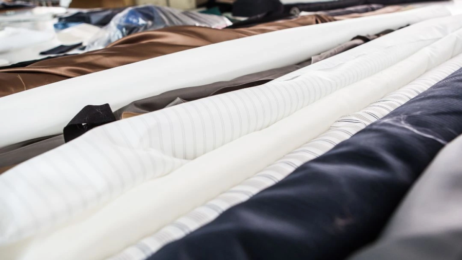 Rolls of different fabric materials, including cotton, polyester, and blended textiles, displayed in a workshop, highlighting texture and finish differences for fabric selection.
